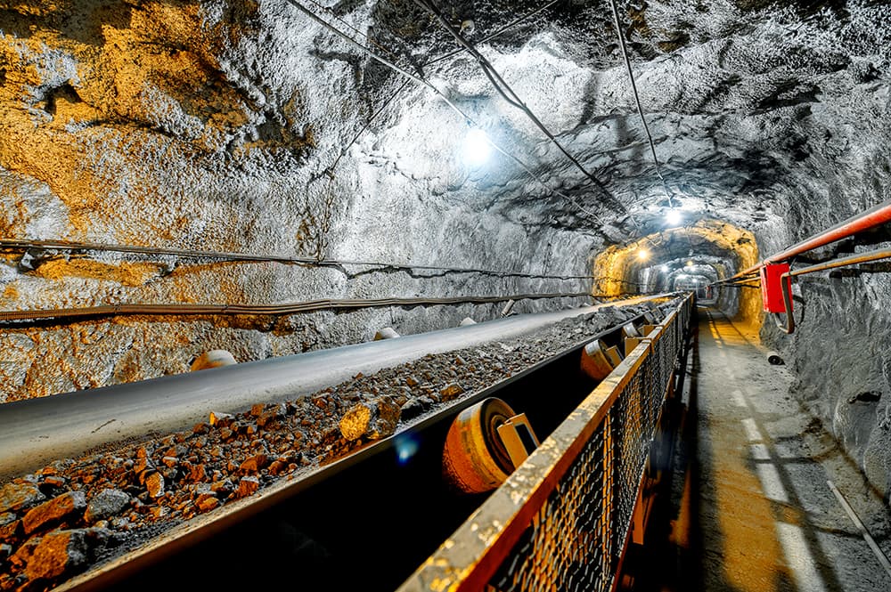 Underground belt conveyor carrying broken mineral material through a mine roadway